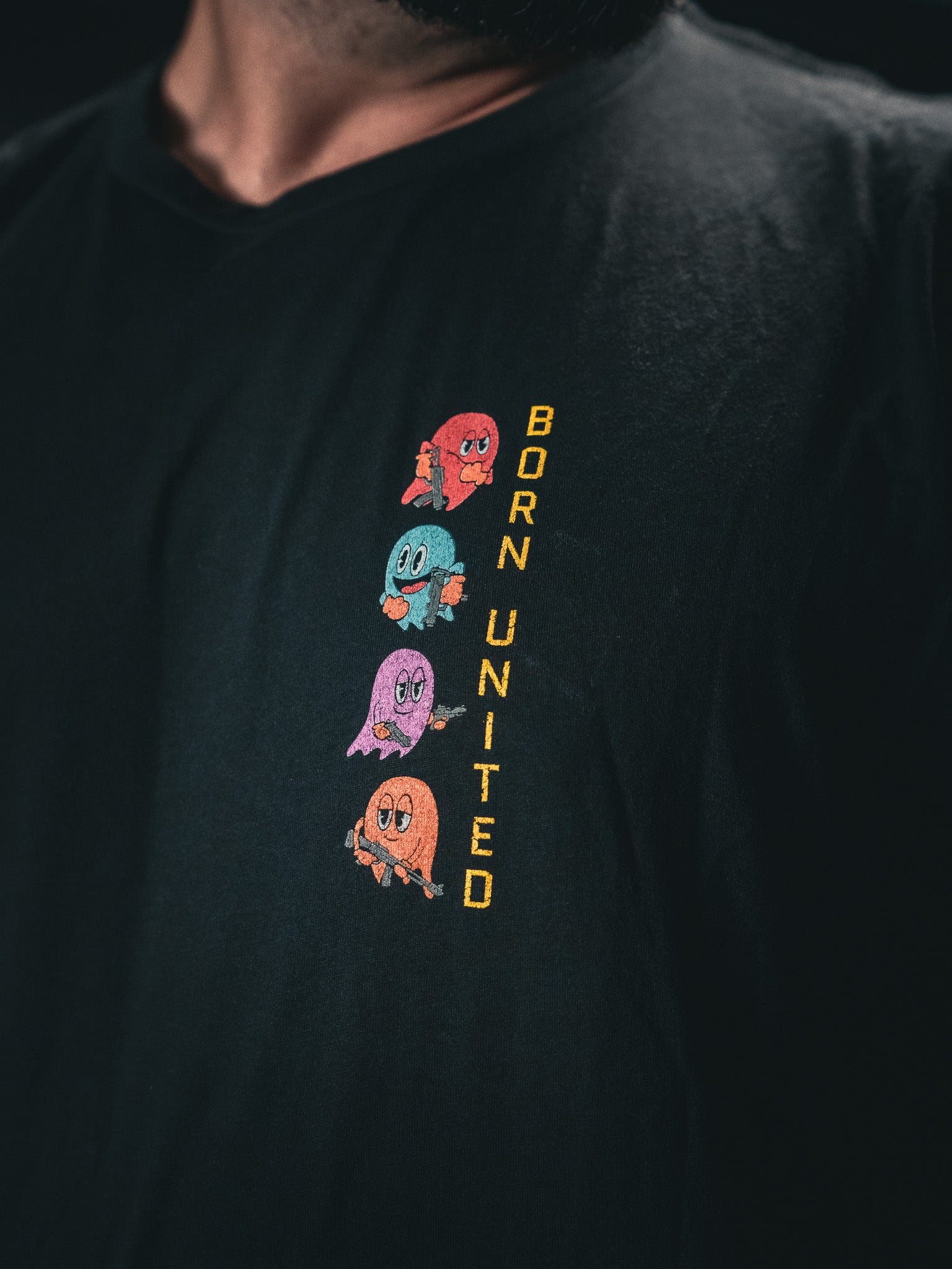 Someone is wearing a Tac-Man (Warehouse) T-shirt from Born United Private Label, featuring colorful ghost-like characters stacked vertically on the left side, with BORN UNITED written alongside.
