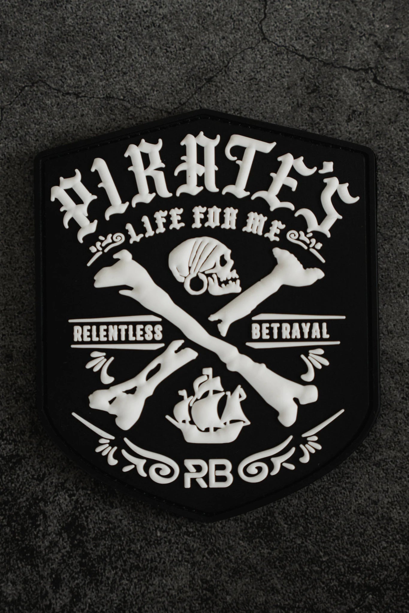 The Pirates Life PVC Patch by Relentless Betrayal features PIRATES with a skull and crossbones above a ship, RELENTLESS BETRAYAL on each side, and LIFE FOR ME with the initials RB, all set on a black patch with white designs.
