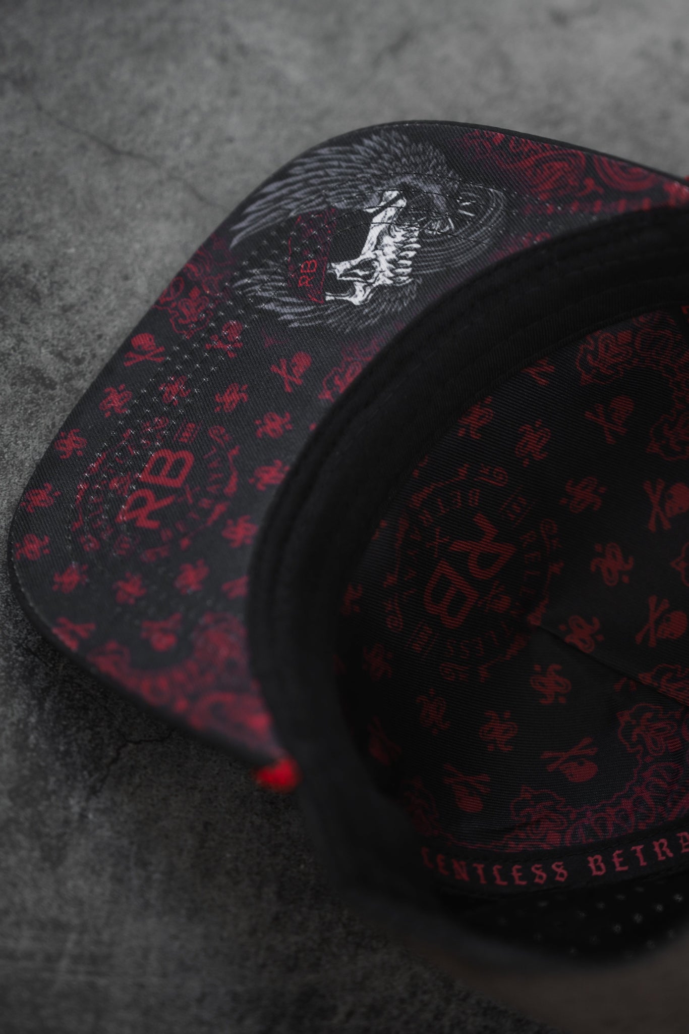 A close-up of the All Gas No Brakes Premium Snapback by Relentless Betrayal, showcasing a black and red design with intricate Asian-inspired motifs and a fierce animal image on the brim. Inside, it features repeated patterns and the letters RBM.
