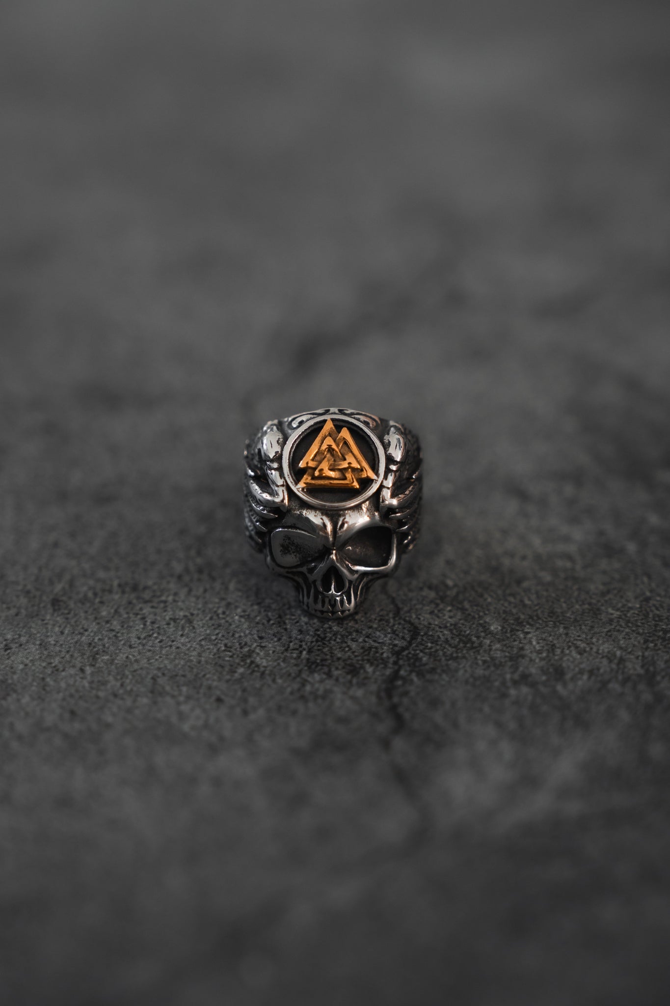 The All Gas No Brakes Ring by Relentless Betrayal features a stainless steel skull with an engraved triangular symbol on its forehead, textured surface, and intricate gold details, creating a bold contrast that embodies youth cultures energy.