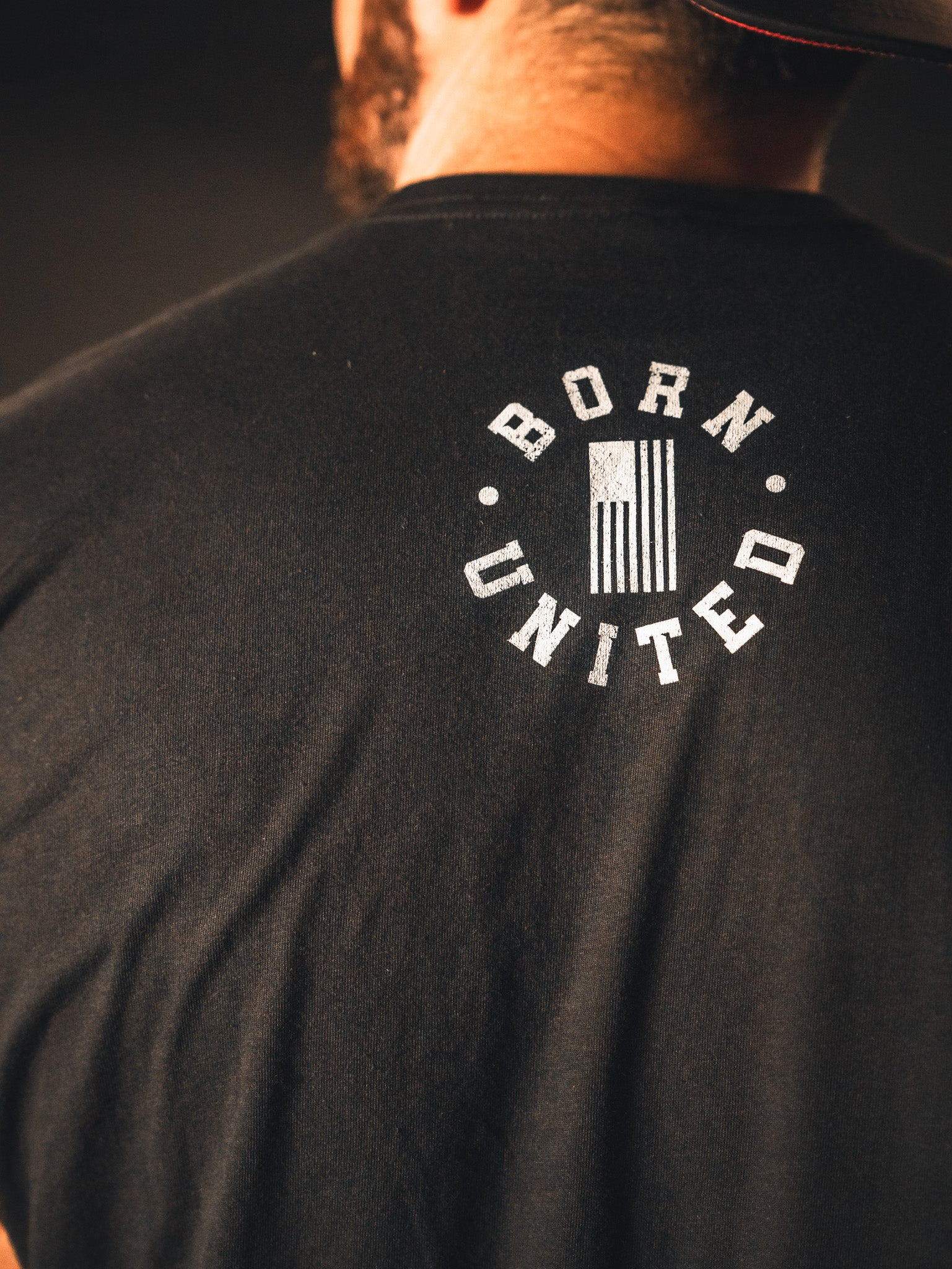 A person proudly stands wearing a black God Over Government T-shirt by Born United Private Label, featuring an American flag. The design embodies the spirit of good conduct and honors the values upheld by governing authorities.