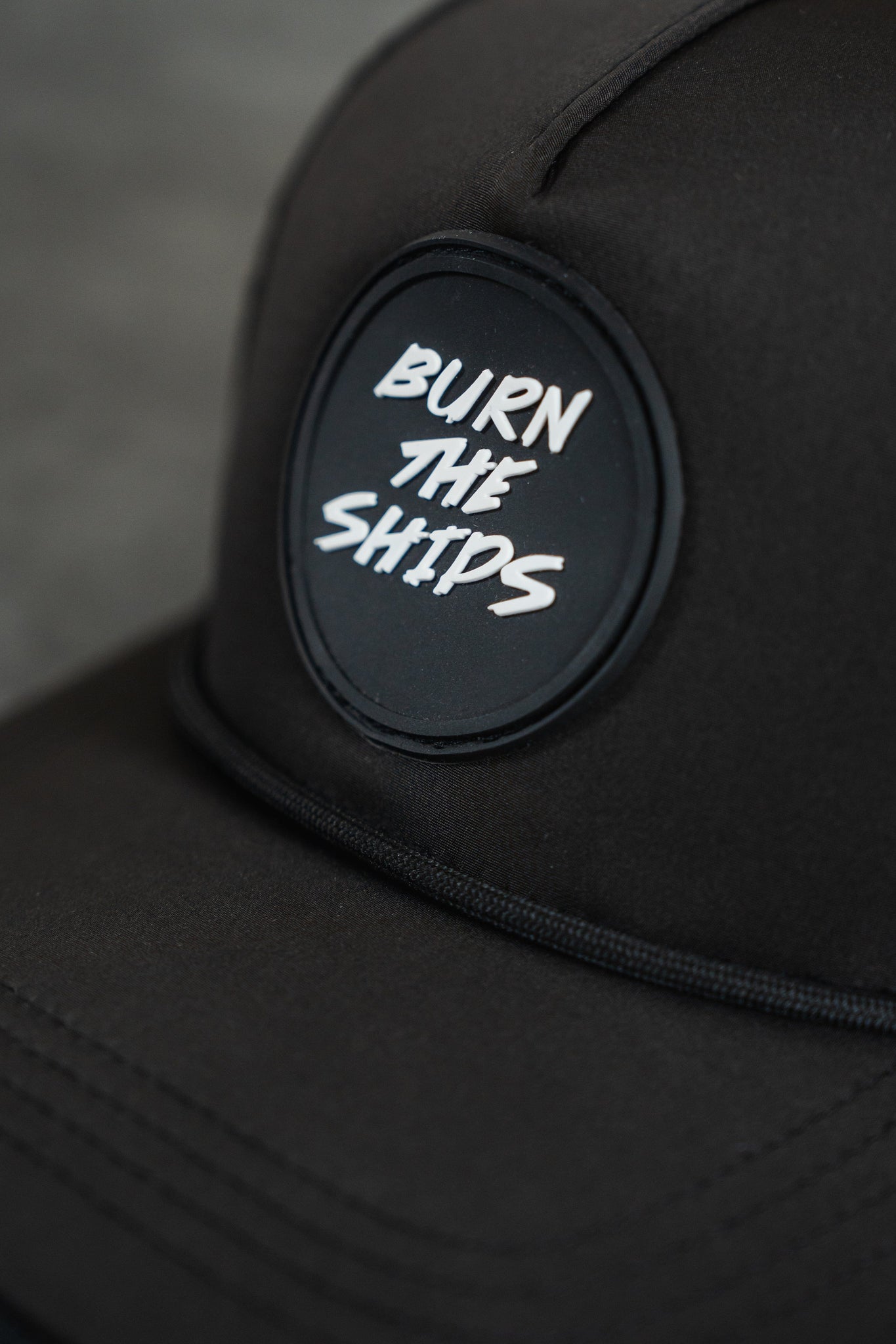 Close-up of the Burn The Ships Black PVC Snapback by Relentless Betrayal, showcasing a round patch with BURN THE SHIPS in white. This water-resistant hat is perfect for the pirate lifestyle, ensuring style and protection on every adventure.