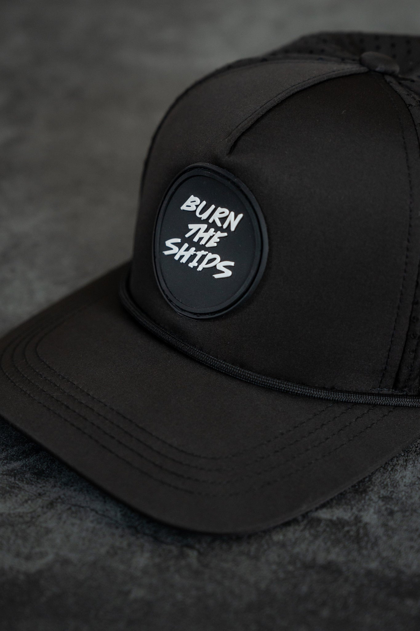The Burn The Ships Black PVC Snapback by Relentless Betrayal features a round BURN THE SHIPS patch in white and is water-resistant, making it perfect for those who embrace the pirate lifestyle.