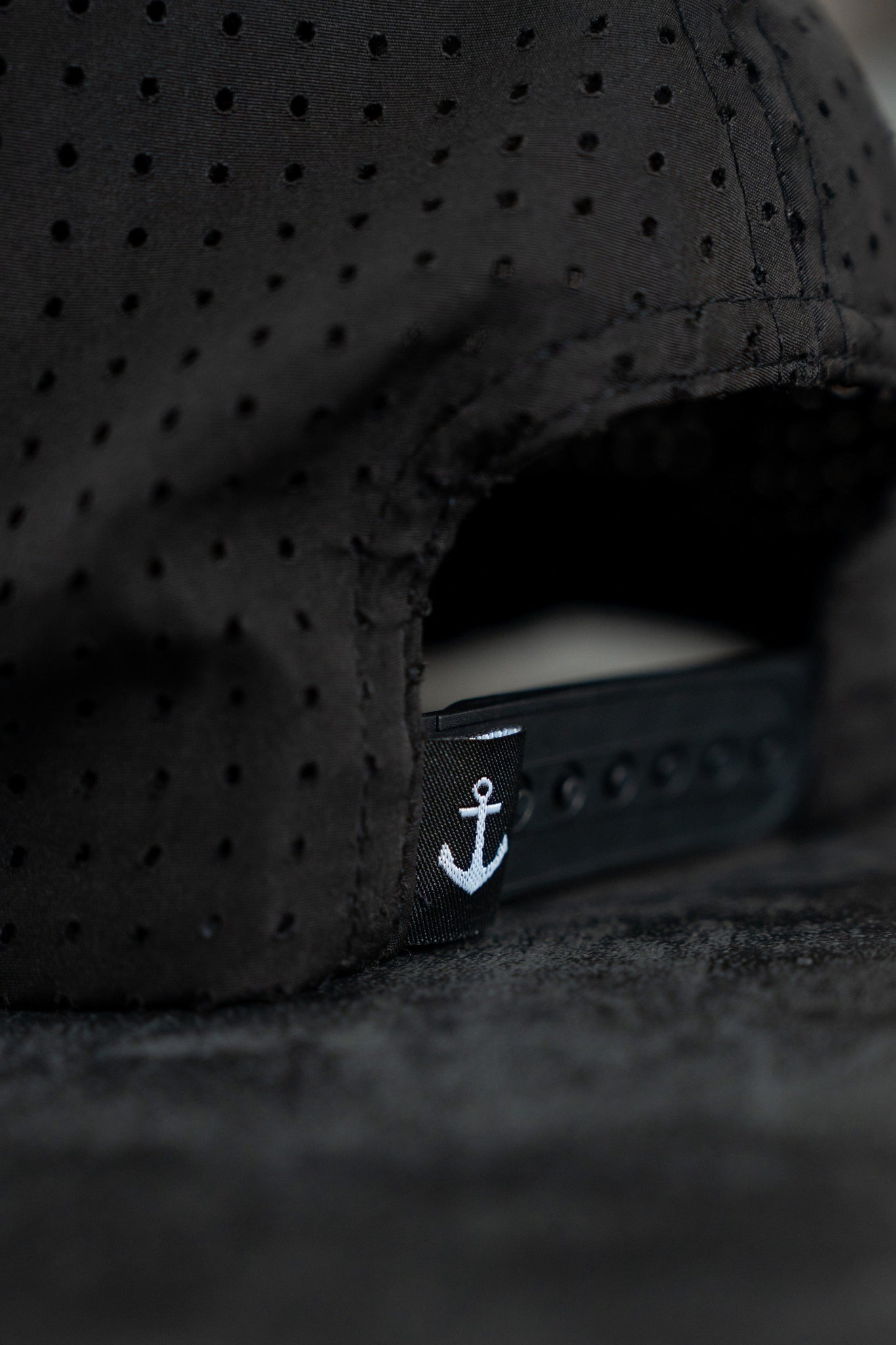 Close-up of the Burn The Ships Black PVC Snapback by Relentless Betrayal, featuring an adjustable strap adorned with a small anchor design symbolic of the pirate lifestyle, set against a textured dark background.