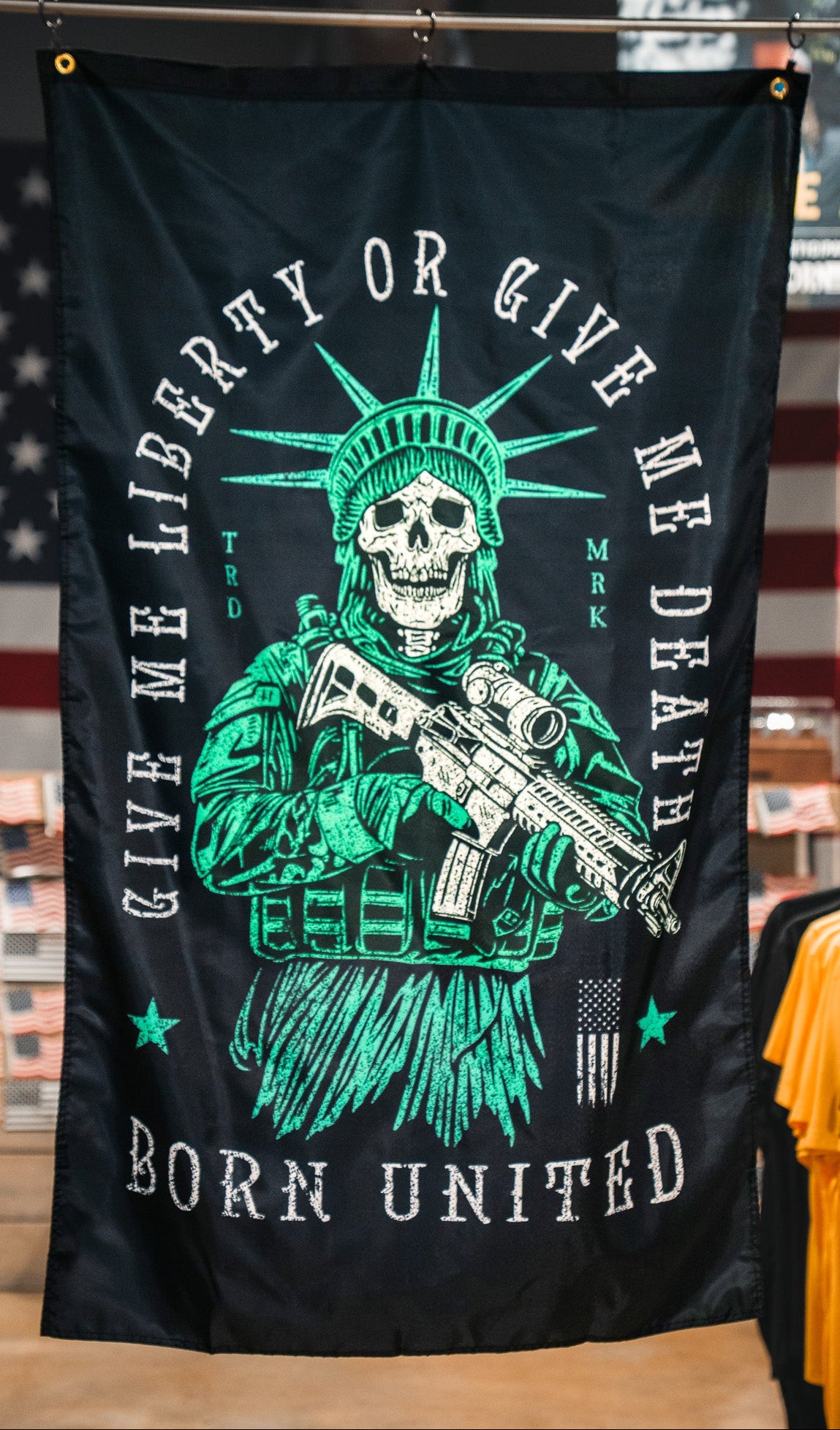 The Liberty or Death Flag by Born United Private Label features a skeleton Statue of Liberty with a rifle and the phrases "Give me liberty or give me death" and "Born United" on a dark background, inspired by American revolutionary flags.
