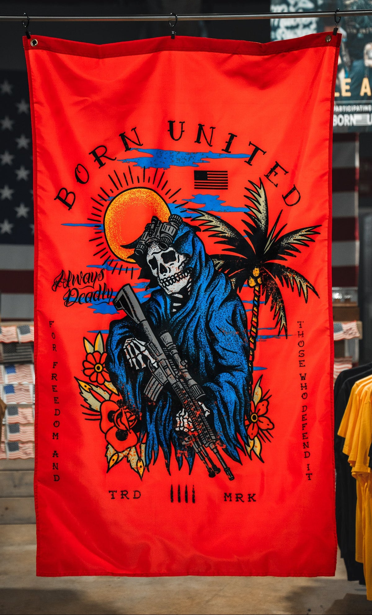 The Always Deadly Flag by Born United Private Label features a grim reaper in a blue hood with a rifle on a red banner, plus sun, palm tree, and American flag accents. "Born United" and "Always Deadly" highlight its patriotic military design.