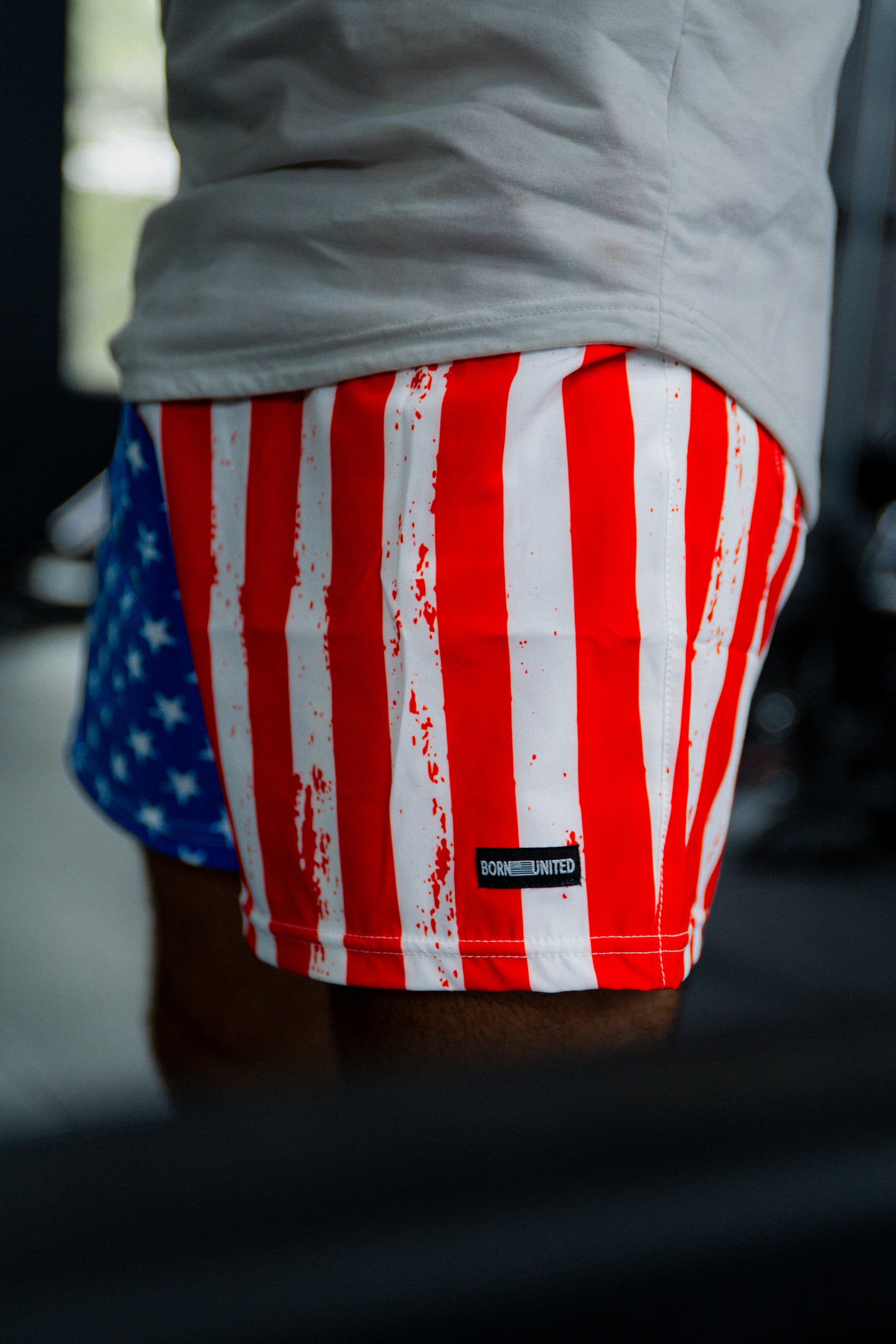 A person wears Born United Private Label Mens Performance Hybrid Shorts 5.5 | Stars & Stripes, featuring an American flag design and quick-drying athletic fabric.