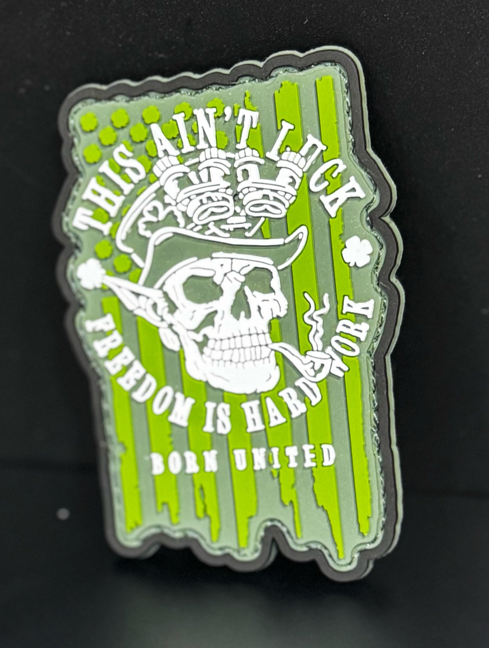 The Freedom Aint Luck PVC Patch by Born United Private Label features a green striped background, a skull in an aviator hat with goggles, and text: THIS AINT LUCK, FREEDOM IS HARD WORK, BORN UNITED.