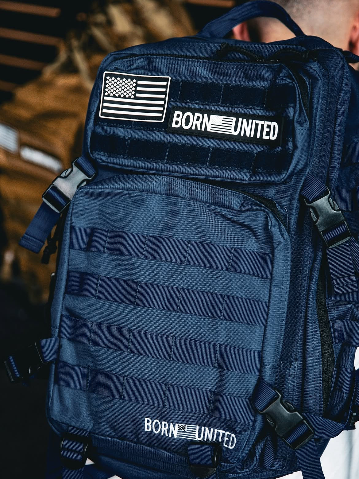 The Navy Blue Tac-Pac - 45L by Born United Private Label features patch designs with a stylized flag and BORN UNITED text. This tactical backpack offers multiple compartments and straps for optimal organization.