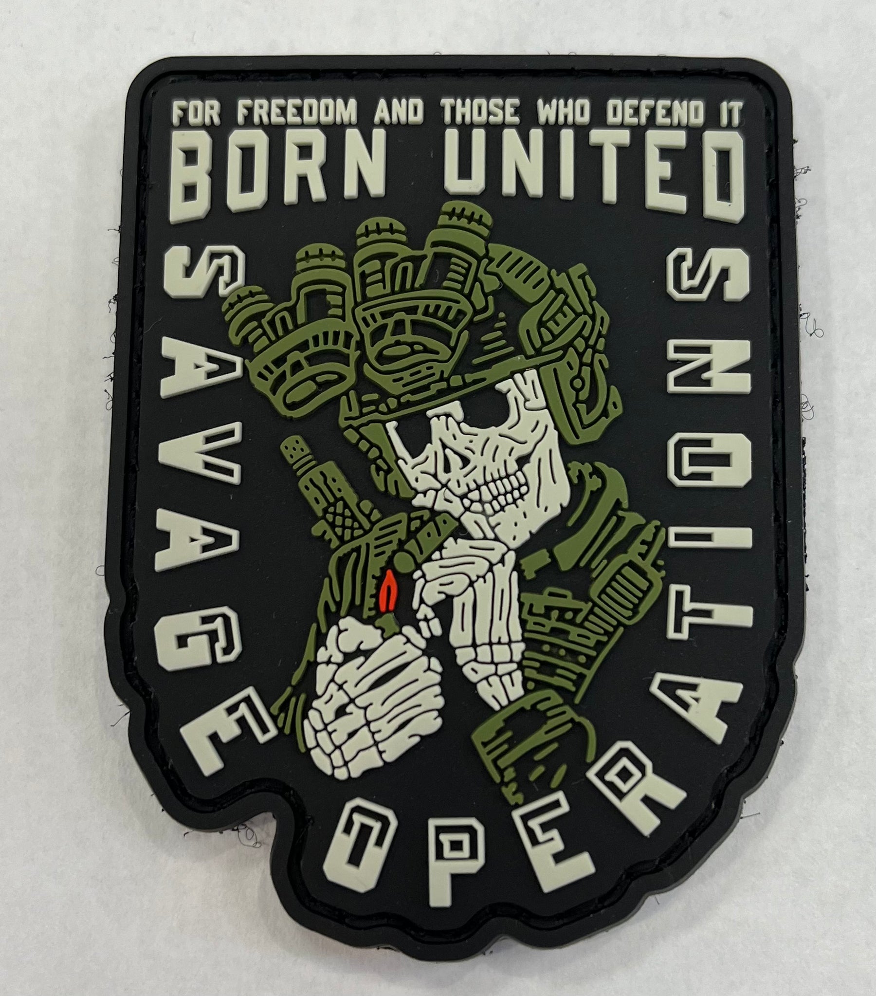 The Savage Operations PVC Patch by Born United Private Label features a skeletal soldier in green combat gear with night vision goggles holding a cigar, alongside the text: FOR FREEDOM AND THOSE WHO DEFEND IT, BORN UNITED, SAVAGE NATIONS, and OPERATIONS.