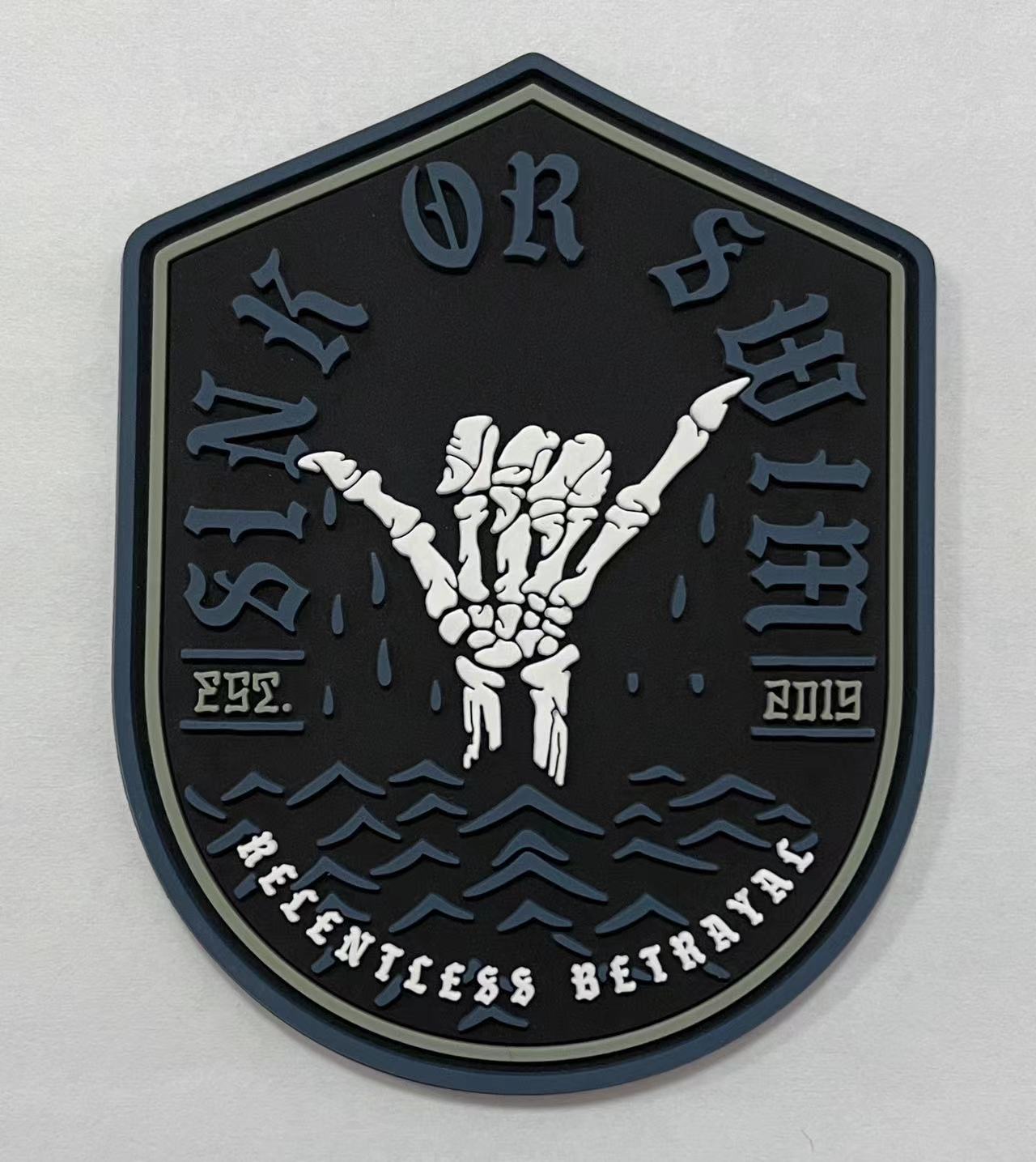 The Sink or Swim PVC Patch by Relentless Betrayal displays a skeleton hand making the rock and roll gesture. Sink or Swim is highlighted above, with Relentless Betrayal below flanked by Est. 2019. Water waves beneath the hand suggest flotation in a pool setting.