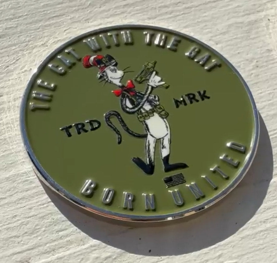The Cat With The Gat Challenge Coin by Born United features a cartoon cat in a tall red and white striped hat, holding a rifle, and wearing a tactical belt. Text reads The Cat With The Gat and Born United, making it a perfect commemorative piece for collectors.