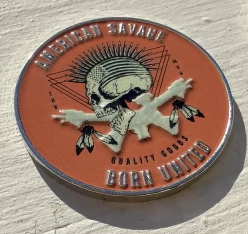 A round, textured American Savage Challenge Coin by Born United Private Label showcases a skull with a mohawk and feathered crossed bones. It features the text American Savage, True Next, Quality Goods, Born United.