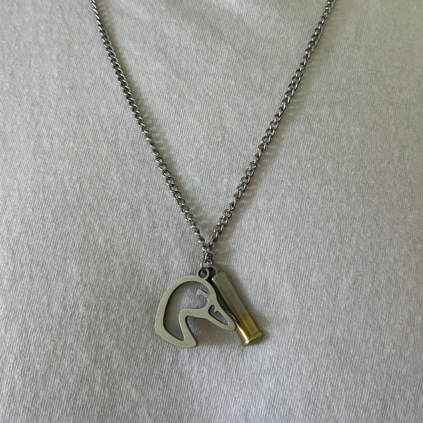 The Mallard Duck Shot necklace from Mucker Bucket showcases a stainless steel pendant with a horse head silhouette and a bullet casing design, beautifully displayed on white fabric. Made in the USA.