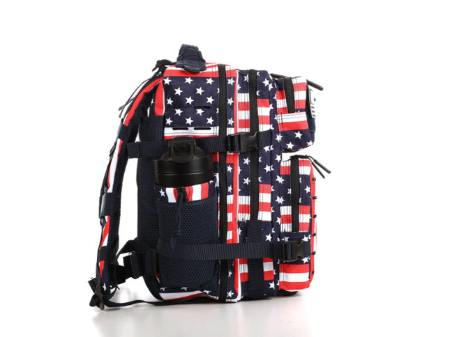 The Ultimate Patriot Special Edition Tac-Pac - 25L by Born United Private Label features an American flag design with stars and stripes, includes multiple compartments with a side pocket for a black bottle, and contrast straps and zippers on a pristine white background.