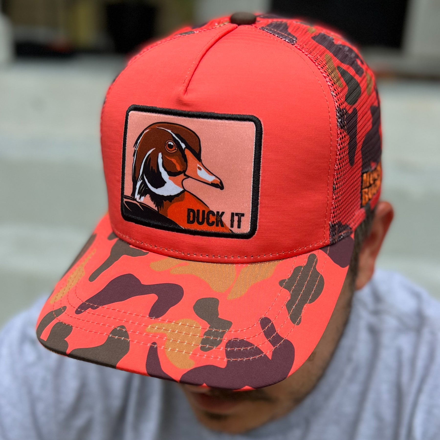mucker bucket - "duck it" orange camo trucker hat on model