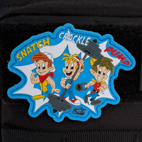 The Tango Charlie Apparel Snatch, Crackle, Pump PVC Patch showcases cartoon characters weightlifting with Snatch Crackle Pump atop a starburst on a blue background. Its versatile design includes an easy Velcro tear-away for quick attachment or removal.