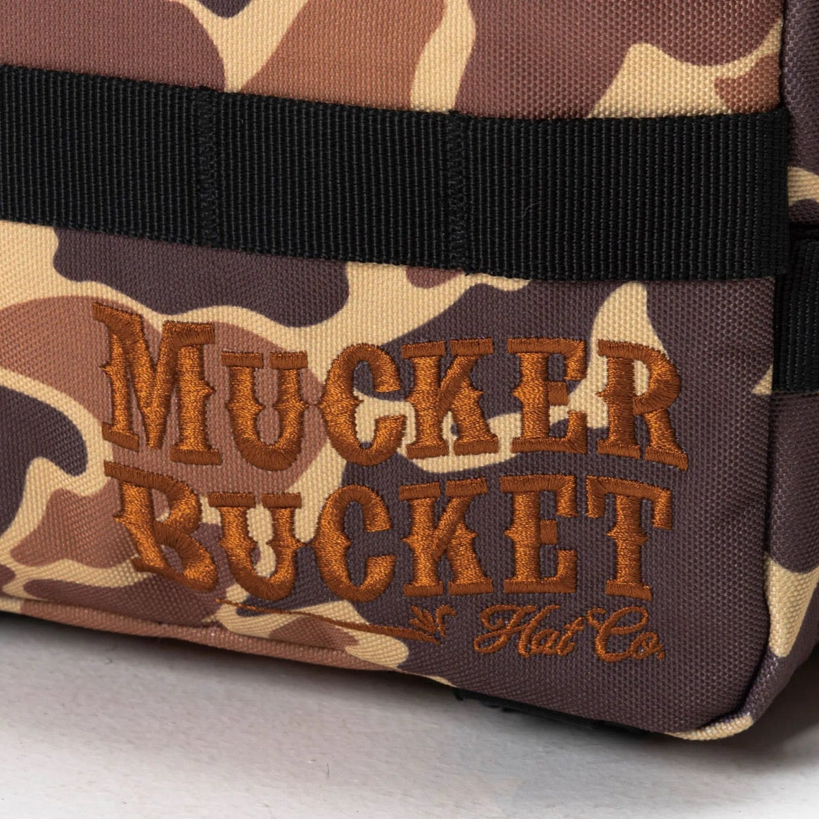 A close-up of the Duck It Limited Edition Tac-Pac - 25L by Mucker Bucket, featuring brown and tan camouflage with bold orange embroidery—an ideal hunting backpack.