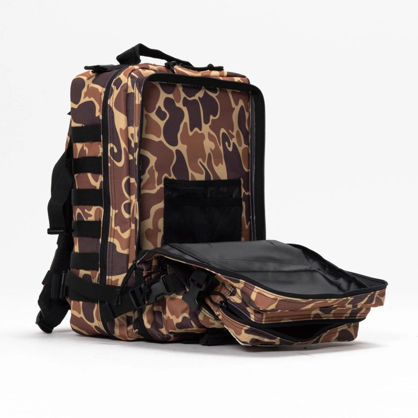 The Mucker Bucket Duck It Limited Edition Tac-Pac - 25L hunting backpack features brown and tan camo with black straps, standing upright on a white background. Its front compartment is unzipped, showing a black interior and mesh pocket.
