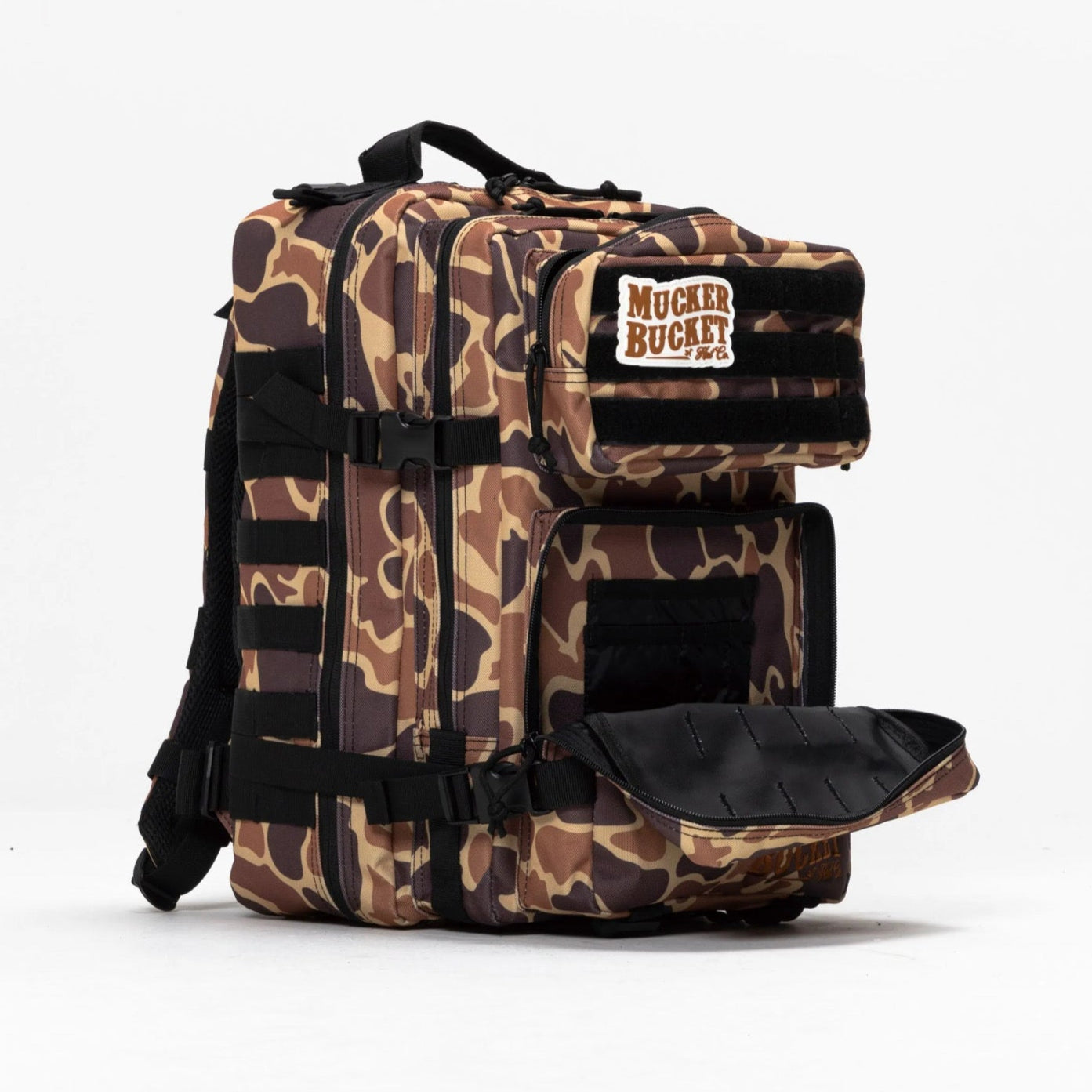 The Mucker Bucket Duck It Limited Edition Tac-Pac - 25L is a camouflage-patterned backpack with multiple compartments, black straps, and a branded patch on the top front pocket. One lower pocket is open to show the interior, set against a plain white background.