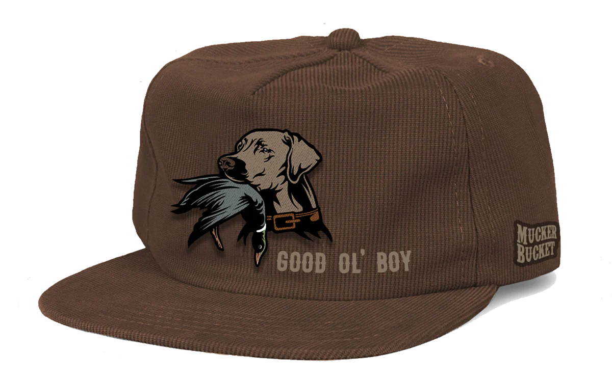The Good Ol Boy Corduroy Bucket by Mucker Bucket is a brown corduroy hat with an embroidered dog holding a duck, GOOD OL BOY on the front, and MUCKER BUCKET on the side. It includes a snapback closure for easy adjustment.