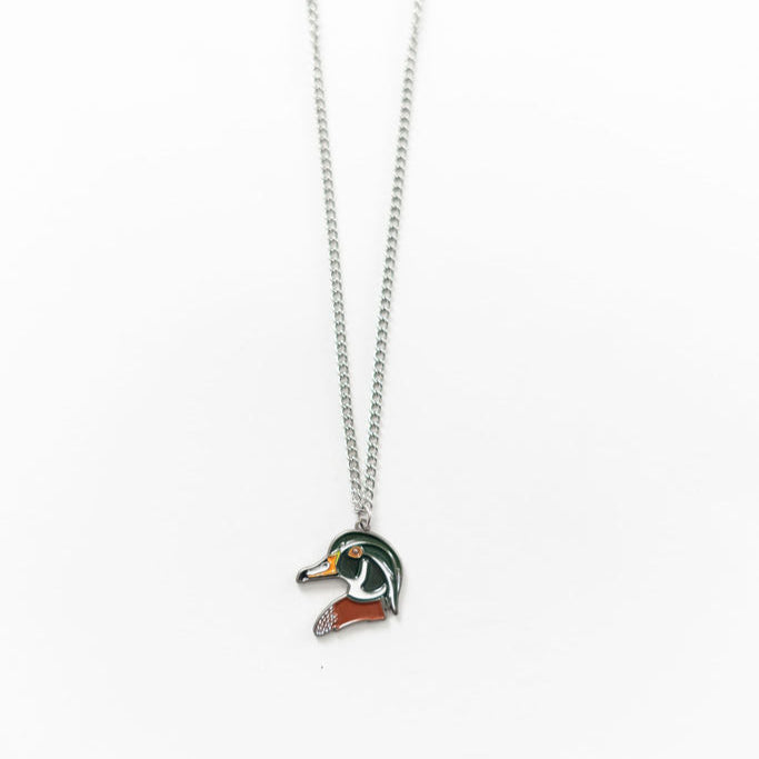 Introducing the Mucker Bucket Wood Duck Necklace, crafted in the USA. This silver chain piece showcases a duck head pendant with green, orange, and black enamel details on a white background.