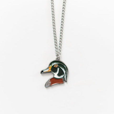 The Mucker Bucket Wood Duck Necklace features a ducks head pendant in vibrant green, orange, and white on a simple stainless steel chain with a white backdrop. Made in the USA, it exudes elegance and charm.