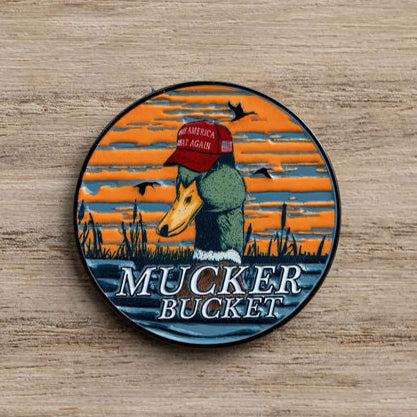 A circular patch features a smart duck in a red hat with an orange sunset backdrop, flying birds, and reeds. Below, on wood, it reads MUCKER BUCKET, capturing the vibe of the Smart Duck Lucky Huntin Coin by Mucker Bucket.