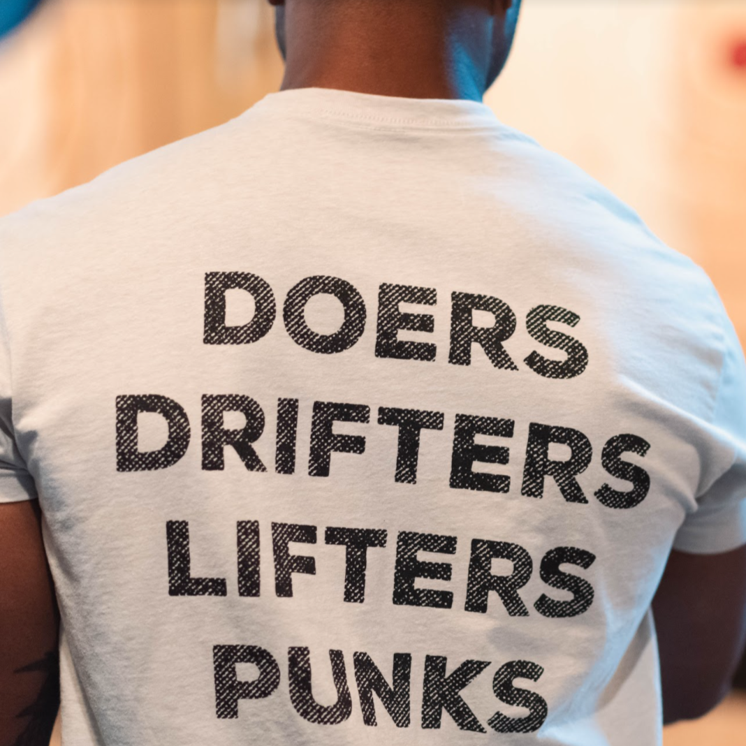 Show your crew spirit in the Doers Drifters Lifters Punks Unisex Tee by Tango Charlie Apparel—a white fitness shirt with bold black lettering on the back. Perfect for athletes and fans alike.