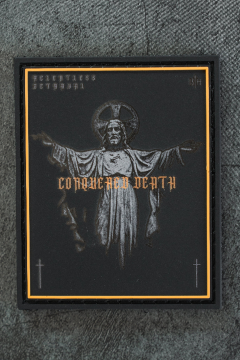 The Conquered Death Patch by 13th features Jesus with outstretched arms, a halo, bold “CONQUERED DEATH” gothic text, black border, subtle crosses, and gold foil details in a striking 3D PVC design.