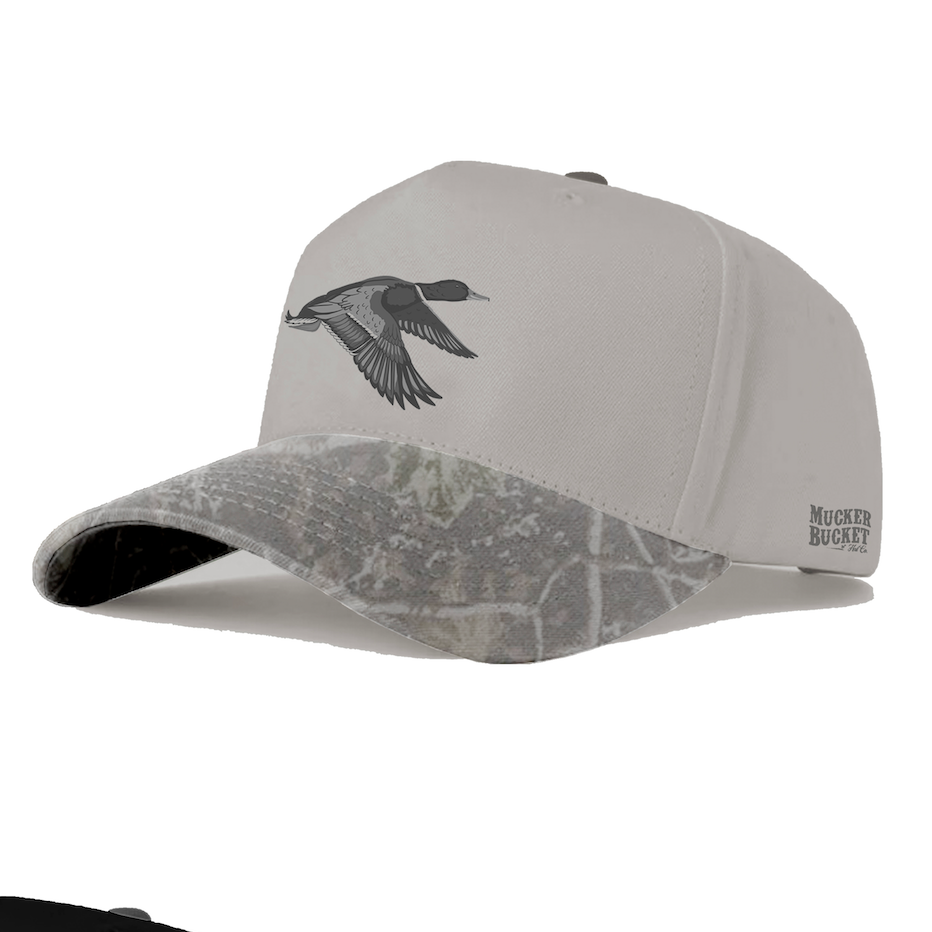 Mallard Gunmetal Deadwood Bucket by Mucker Bucket: a gray baseball cap featuring detailed flying duck embroidery on the front, MUCKER BUCKET text on the side, and a camo brim—perfect for that authentic Mallard Season flair.