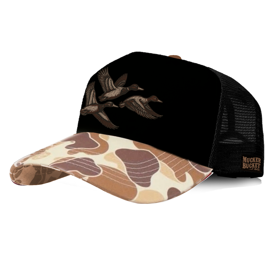 Introducing the Duck Boss Trucker Bucket by Mucker Bucket—a trucker snapback hat featuring a black crown with flying ducks, a brown camo-patterned brim, detailed patch embroidery, and a black mesh back with a signature Mucker Bucket label on the side.