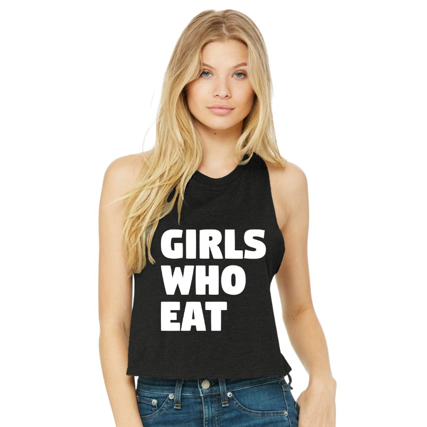 A young woman with long blonde hair models the Tango Charlie Apparel Girls Who Eat Crop Tank—a comfy, sleeveless black top featuring bold white lettering—while standing against a plain white background and looking at the camera.