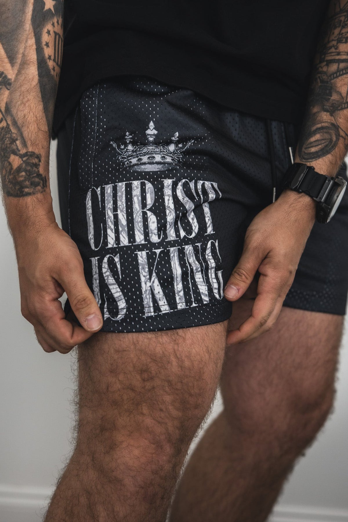 Wearing 13th Men's Mesh Lifestyle Shorts | 5.5"- Christ is King, featuring bold white text and a crown graphic, this look highlights arm tattoos—stylish mesh shorts that make a statement for any casual men's outfit.