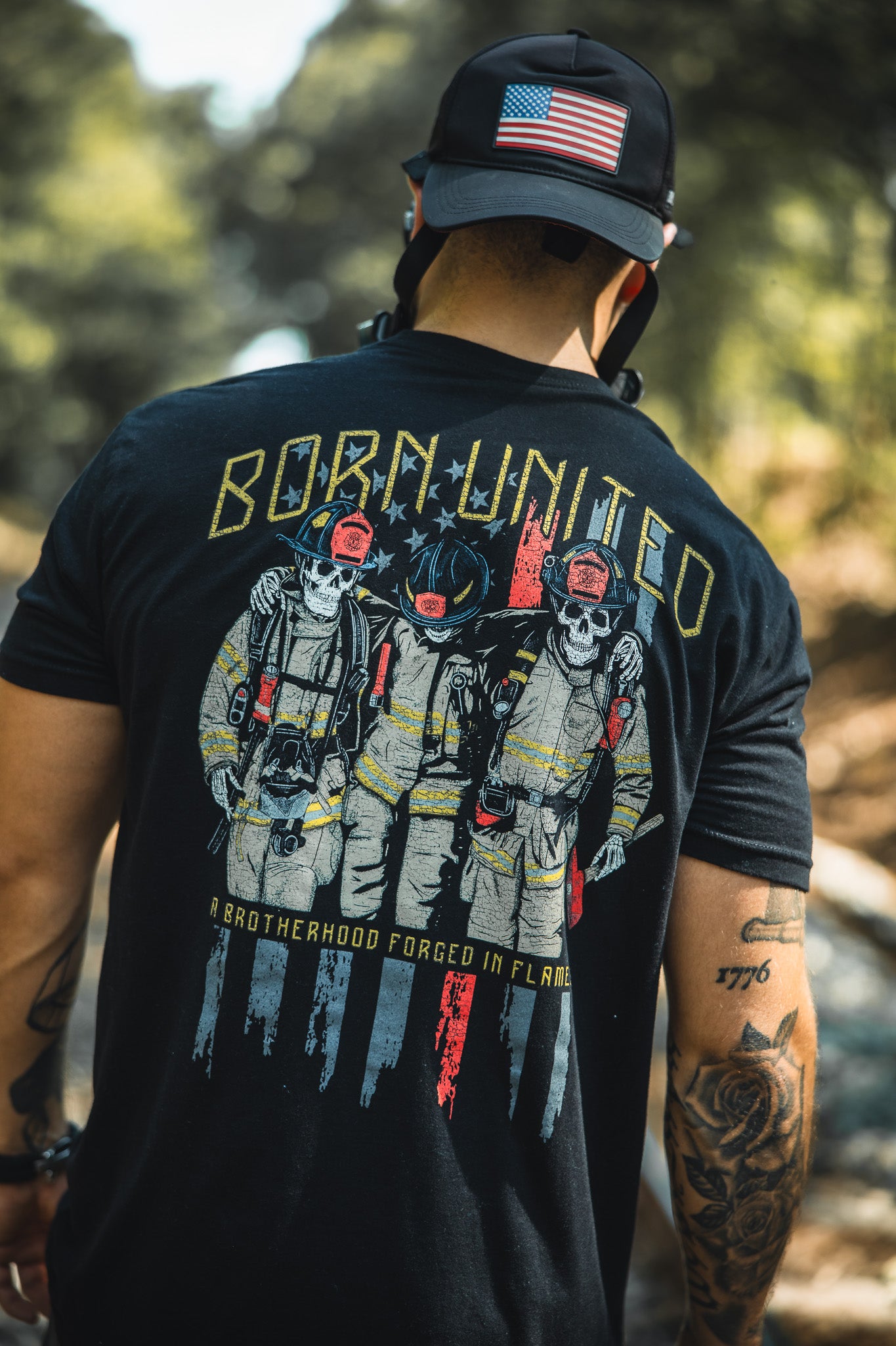 A man wearing a Born United Private Label Brotherhood Forged In Flames black cap with an American flag patch and matching T-shirt featuring three skeleton firefighters, celebrating unity in firefighting.