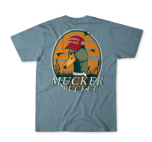The Youth Smart Duck Premium Tee by Mucker Bucket is a blue T-shirt showing a duck in a red MAGA hat standing in reeds with flying birds behind, plus MUCKER BUCKET beneath the image.