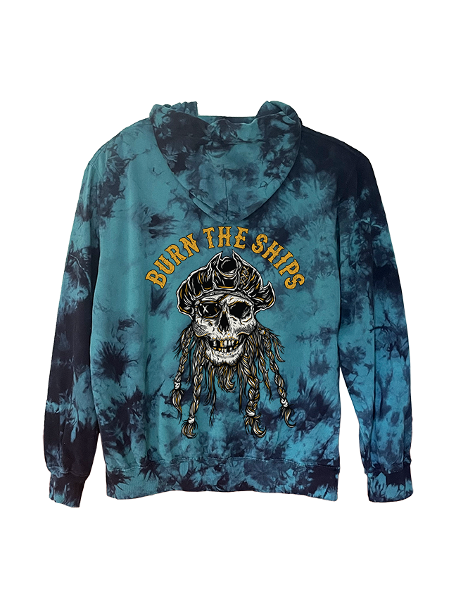 The Burn The Ships Tie Dye Hoodie by Relentless Betrayal is a unisex hoodie, crafted from a soft cotton-polyester blend, showcasing blue and black tones. A skull in a pirate hat with braided hair appears on the back under bold yellow Burn the Ships lettering.
