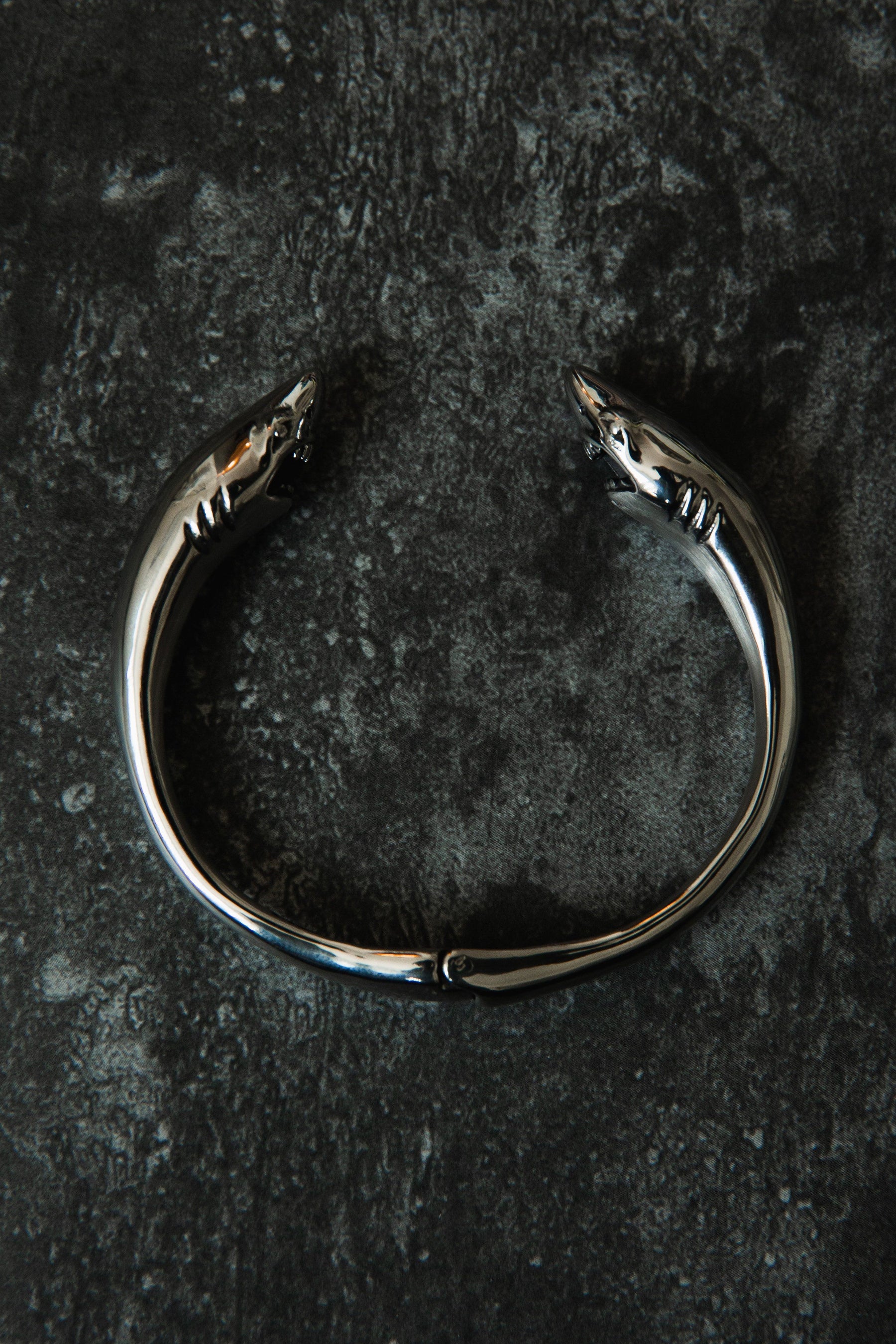Introducing the Relentless Betrayal Shark Bait Bracelet: a sleek, stainless steel accessory featuring dual shark heads on a textured dark surface, complete with a lifetime warranty for unmatched style and durability.