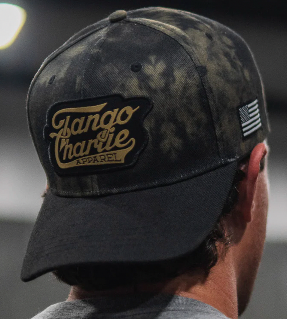 Sporting the TCA Tie Dye Snapback by Tango Charlie Apparel, this cap features a camo-pattern flat bill, Tango Charlie Apparel stitched on the back, and an American flag patch on the side. Its snapback enclosure ensures comfort with hair peeking out beneath.