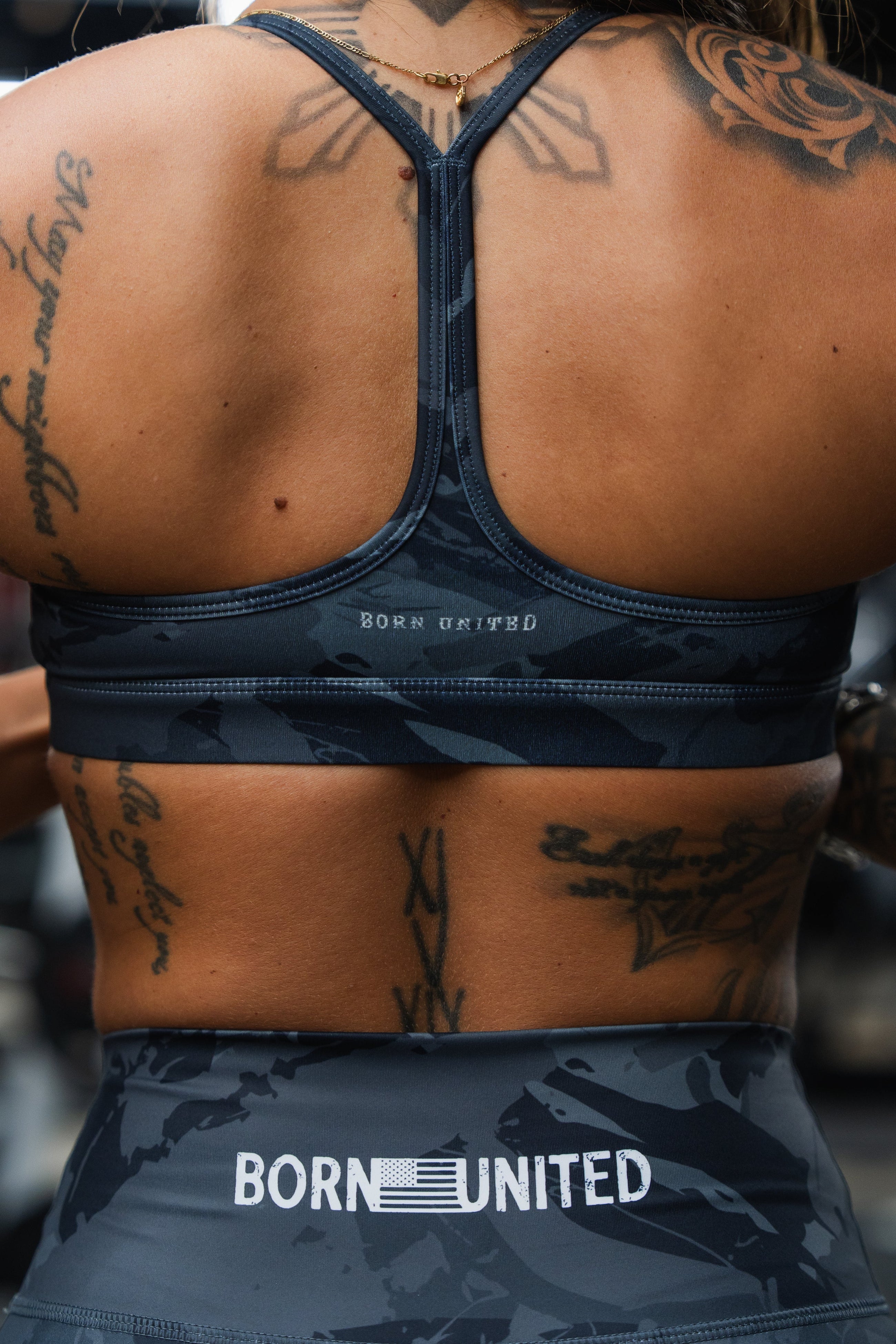 A person wearing a black shirt with bold white letters and camouflage pants featuring black rifle illustrations, pulling the waistband slightly to show the fabric design.