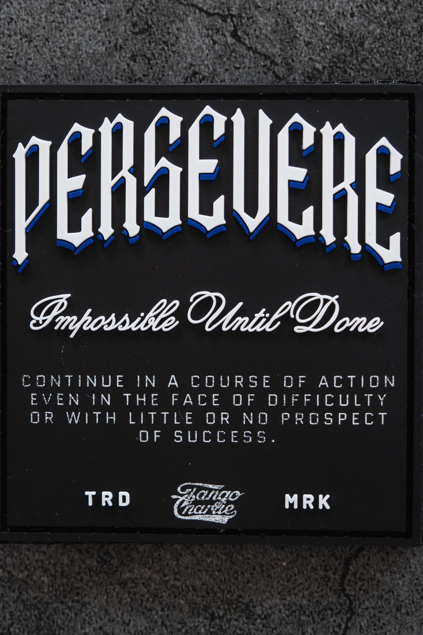 A black sign reads: PERSEVERE. Impossible Until Done. Continue in a course of action even in the face of difficulty or with little or no prospect of success. TRD MRK.