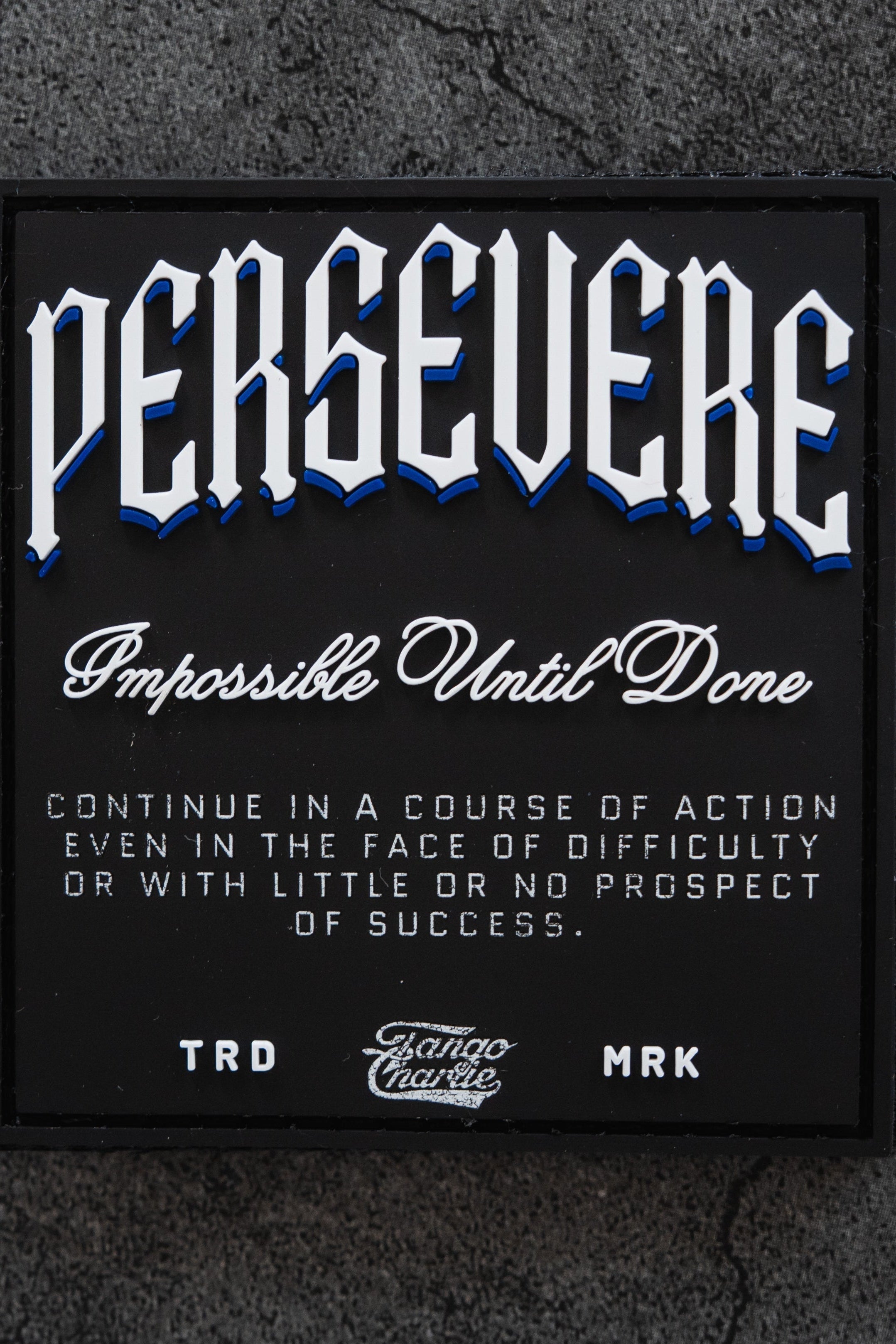 A black sign reads: PERSEVERE. Impossible Until Done. Continue in a course of action even in the face of difficulty or with little or no prospect of success. TRD MRK.