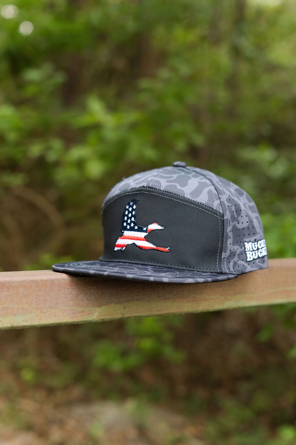 Silhouette of a person aiming a bow at a deer at sunset, with birds flying in the sky and the “Mucker Bucket Hat Co.” logo beside the deer.