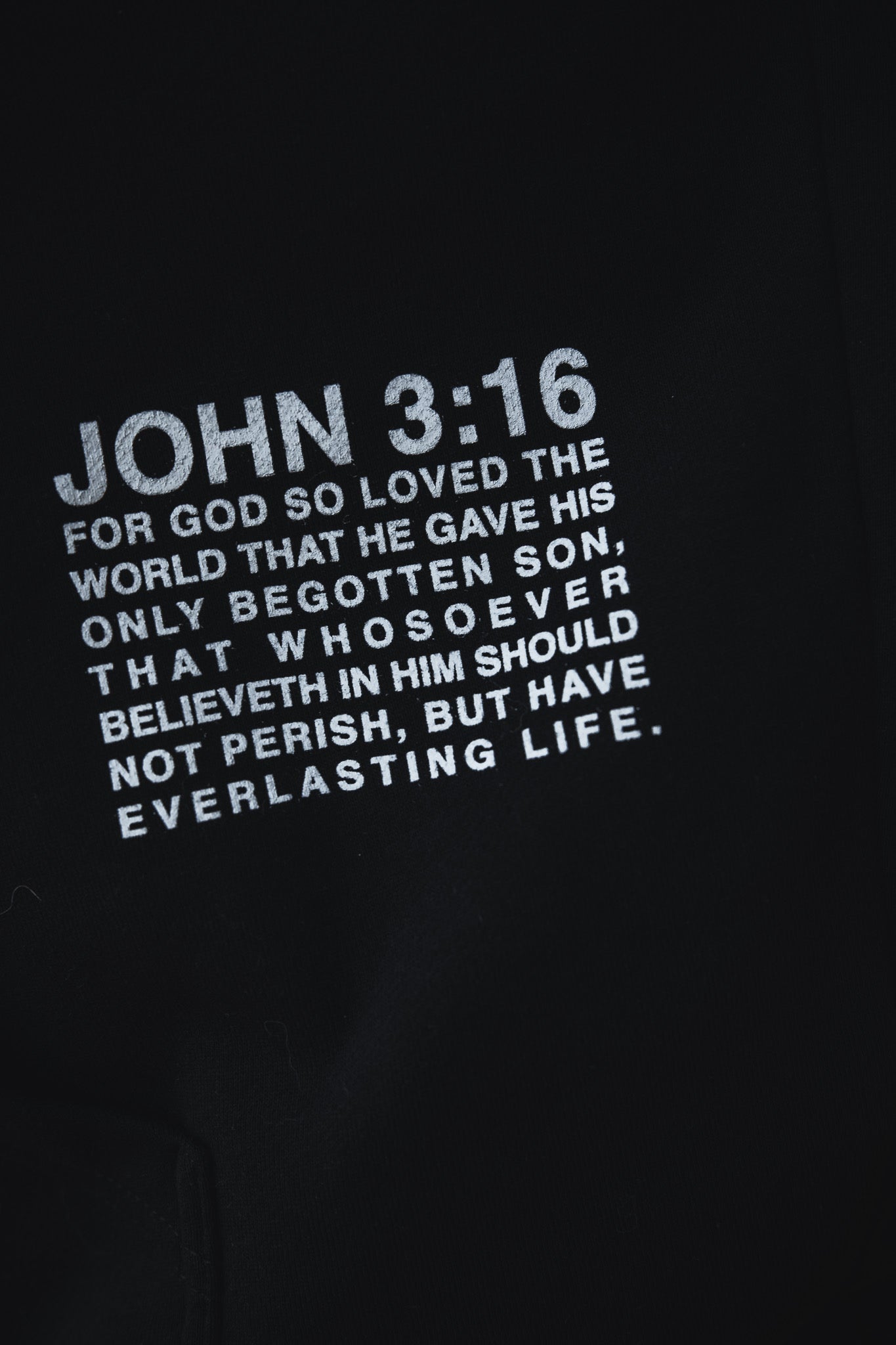 Close-up of text on a black fabric reading JOHN 3:16 For God so loved the world that he gave his only begotten son, that whosoever believeth in him should not perish, but have everlasting life.