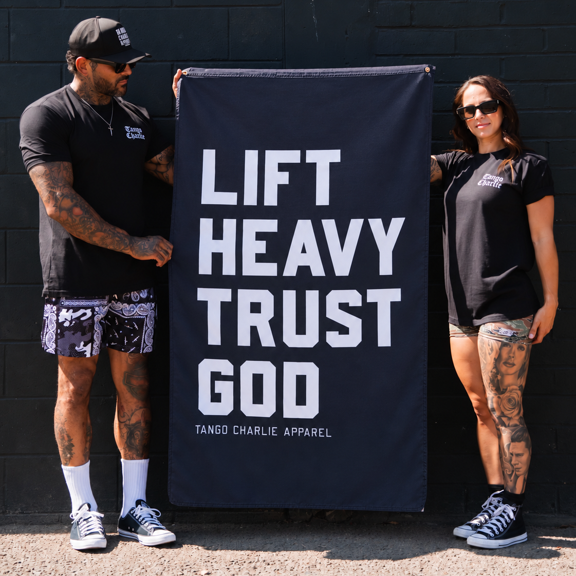 A man and a woman holding a large black Lift Heavy. Trust God. Flag with white lettering.