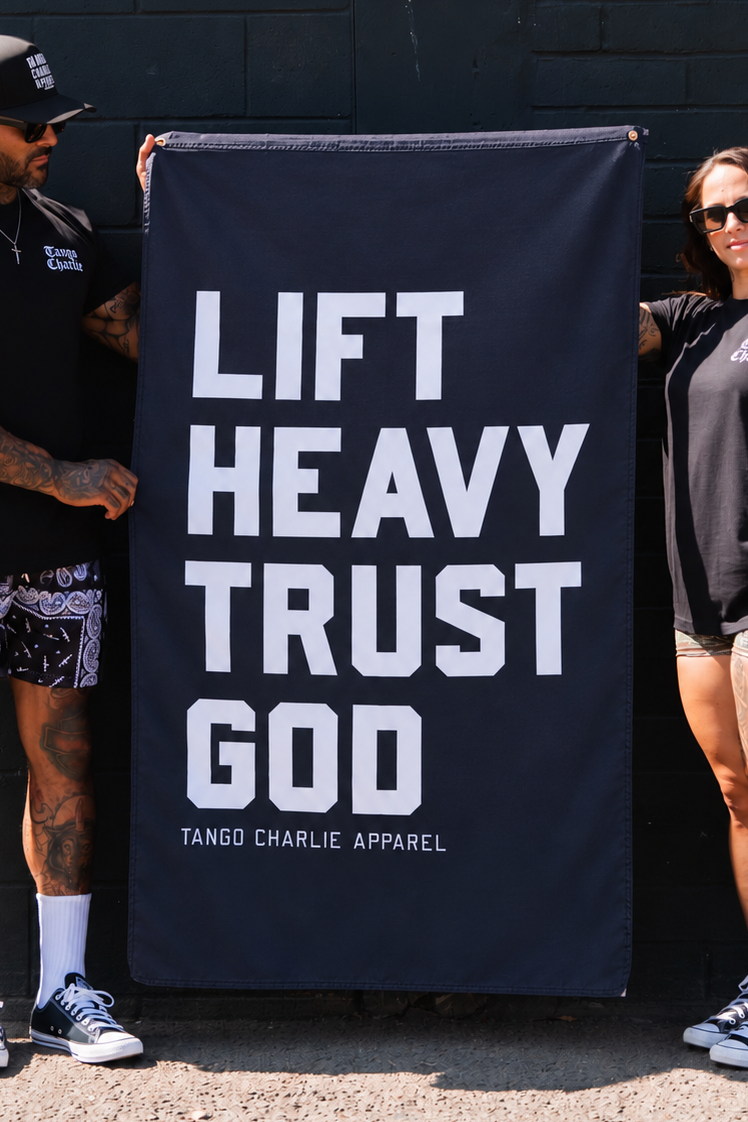A man and a woman holding a large black Lift Heavy. Trust God. Flag with white lettering.