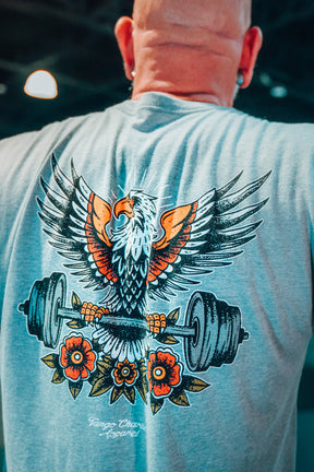 Person wearing a gray t-shirt with an eagle and barbell design on the back, standing in a gym.