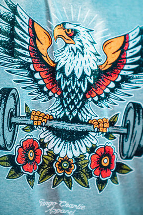 T-shirt with an eagle lifting a barbell and flowers design on a light blue background.