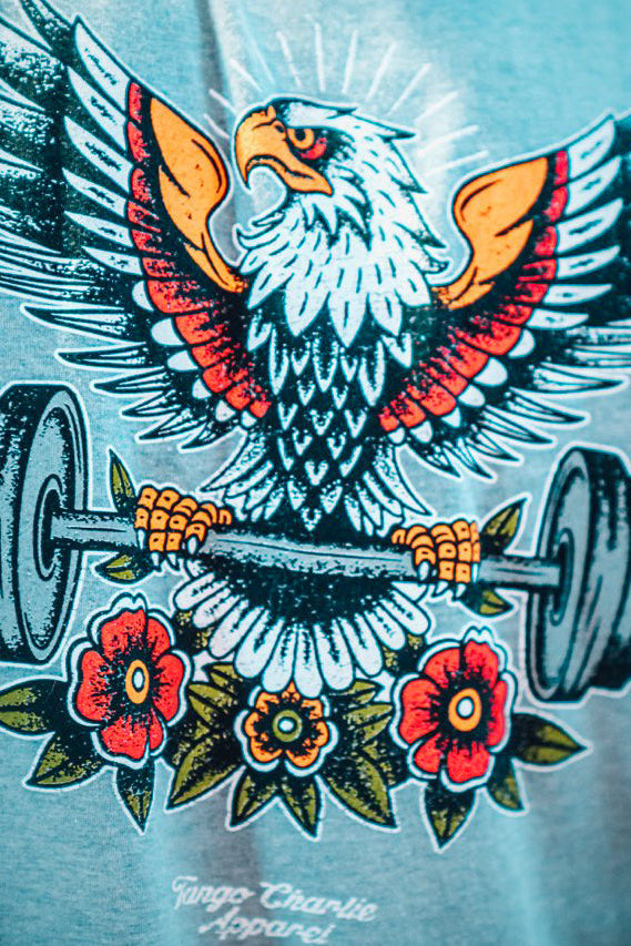 T-shirt with an eagle lifting a barbell and flowers design on a light blue background.