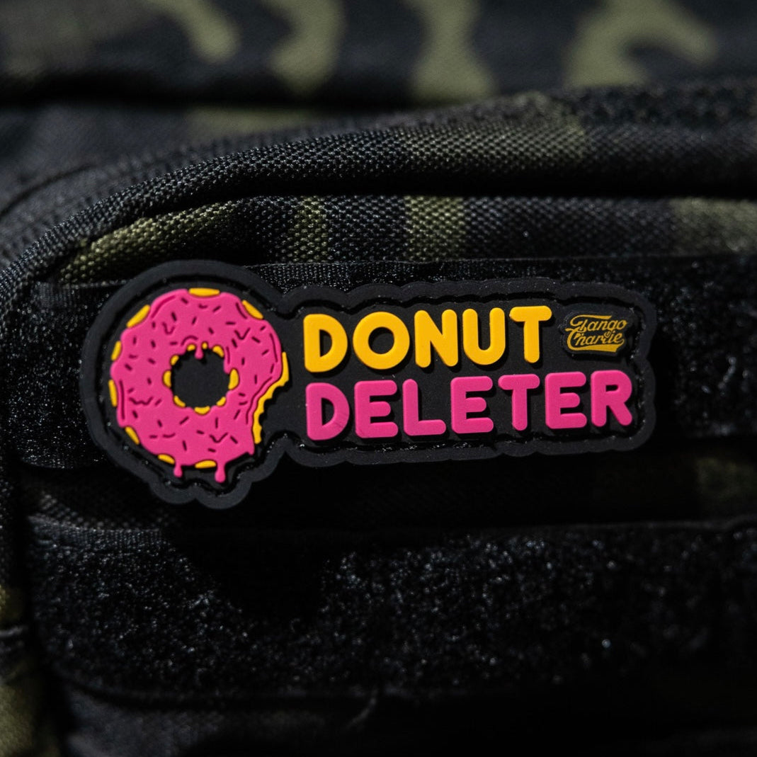 The Donut Deleter - Patch by Tango Charlie Apparel is a 3-inch 3D PVC patch with a pink sprinkled donut and “DONUT DELETER” in yellow/pink, plus a small Giant Mouse logo. It attaches to fabric surfaces with Velcro backing.